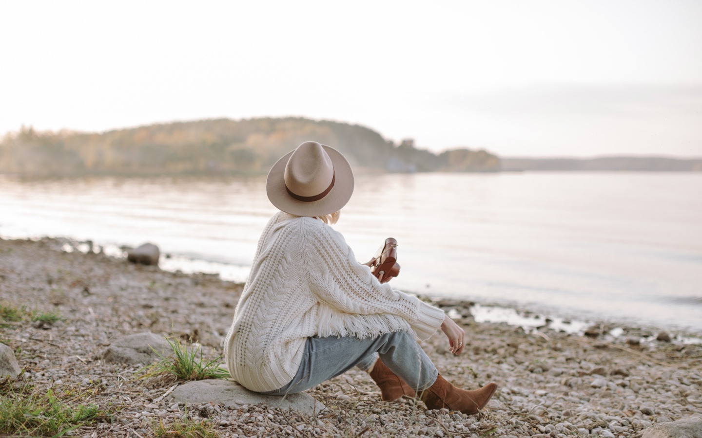 Woman Sitting On Shore Taking Pictures At Sunset