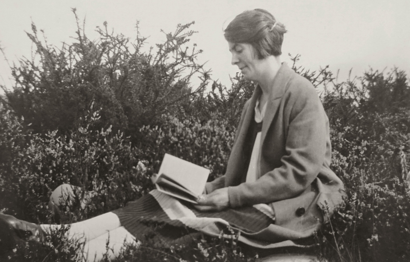 grayscale image of woman reading in a field