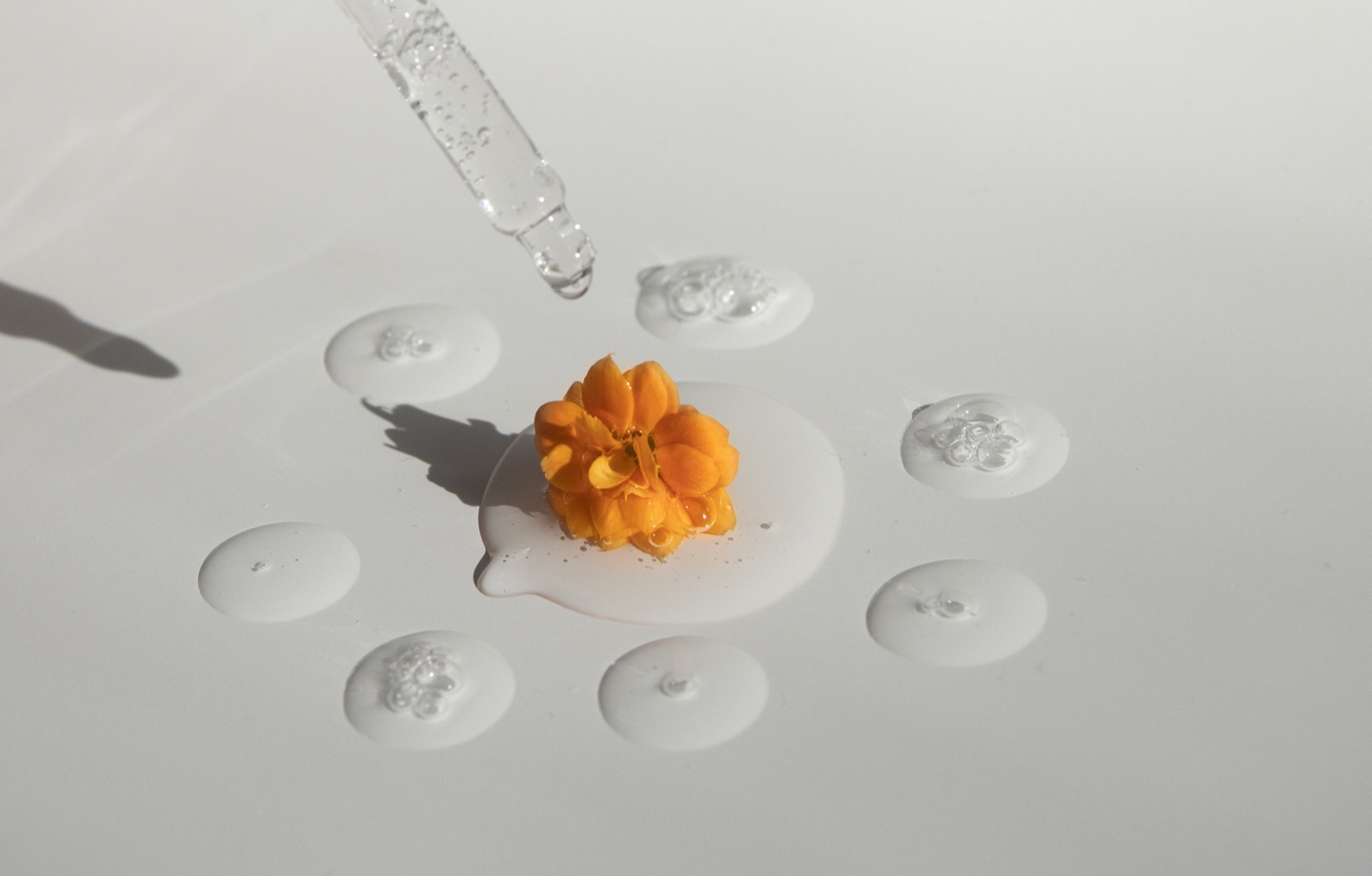 pipette with transparent essence and yellow flower on white surface