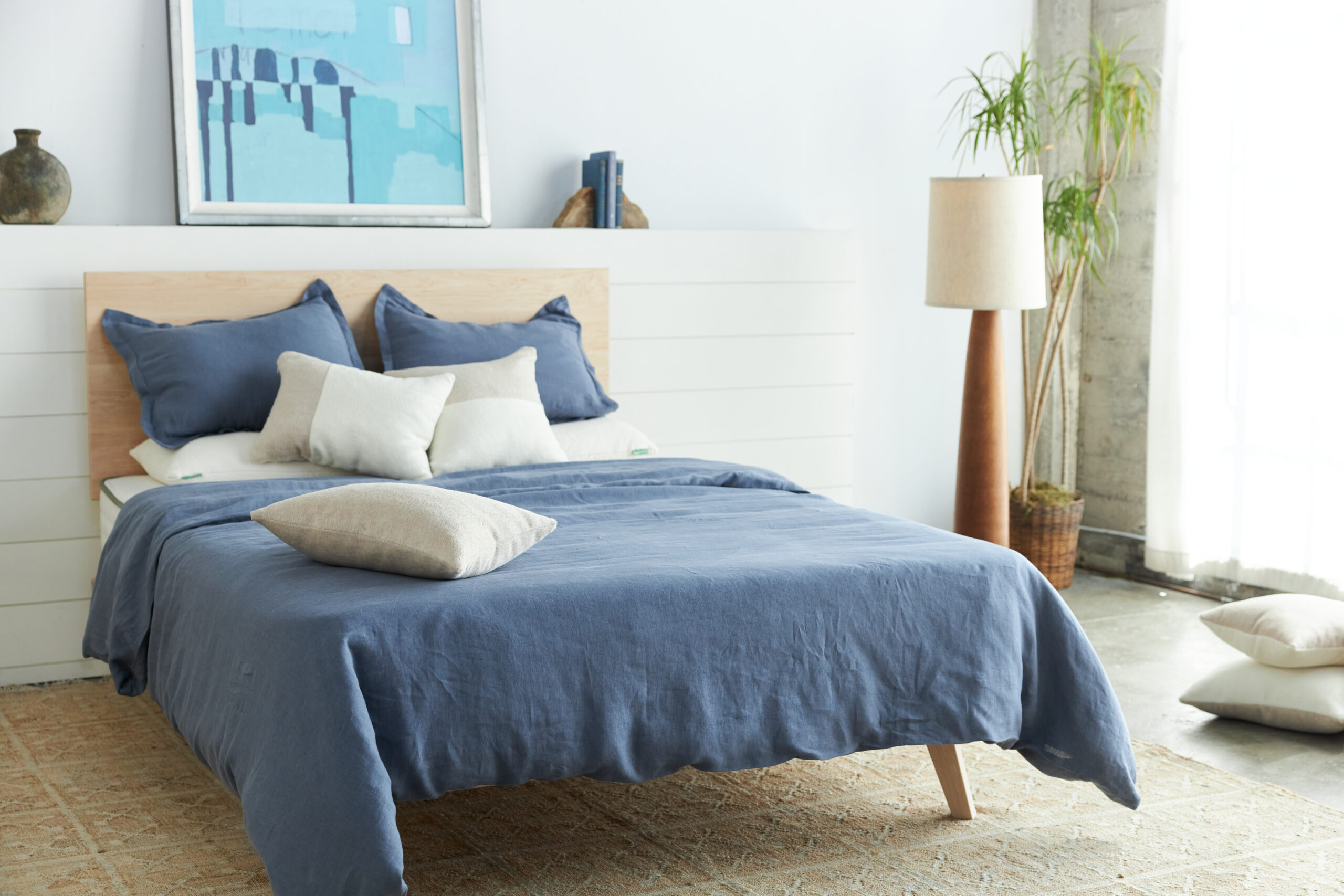 avocado mattress on midcentury modern bed frame covered in indigo linen sheets with alpaca throw pillows