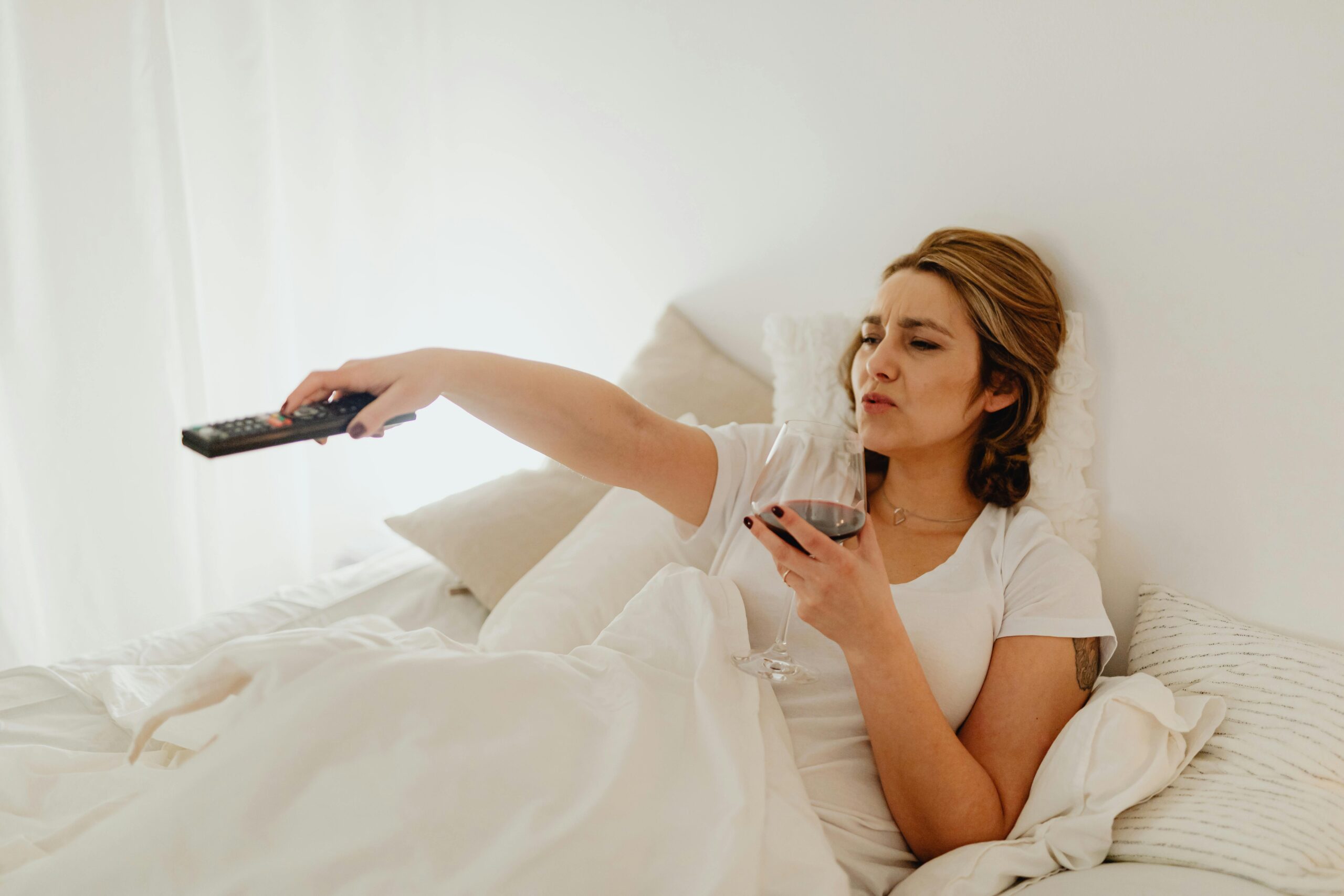 woman in bed with remote and wine